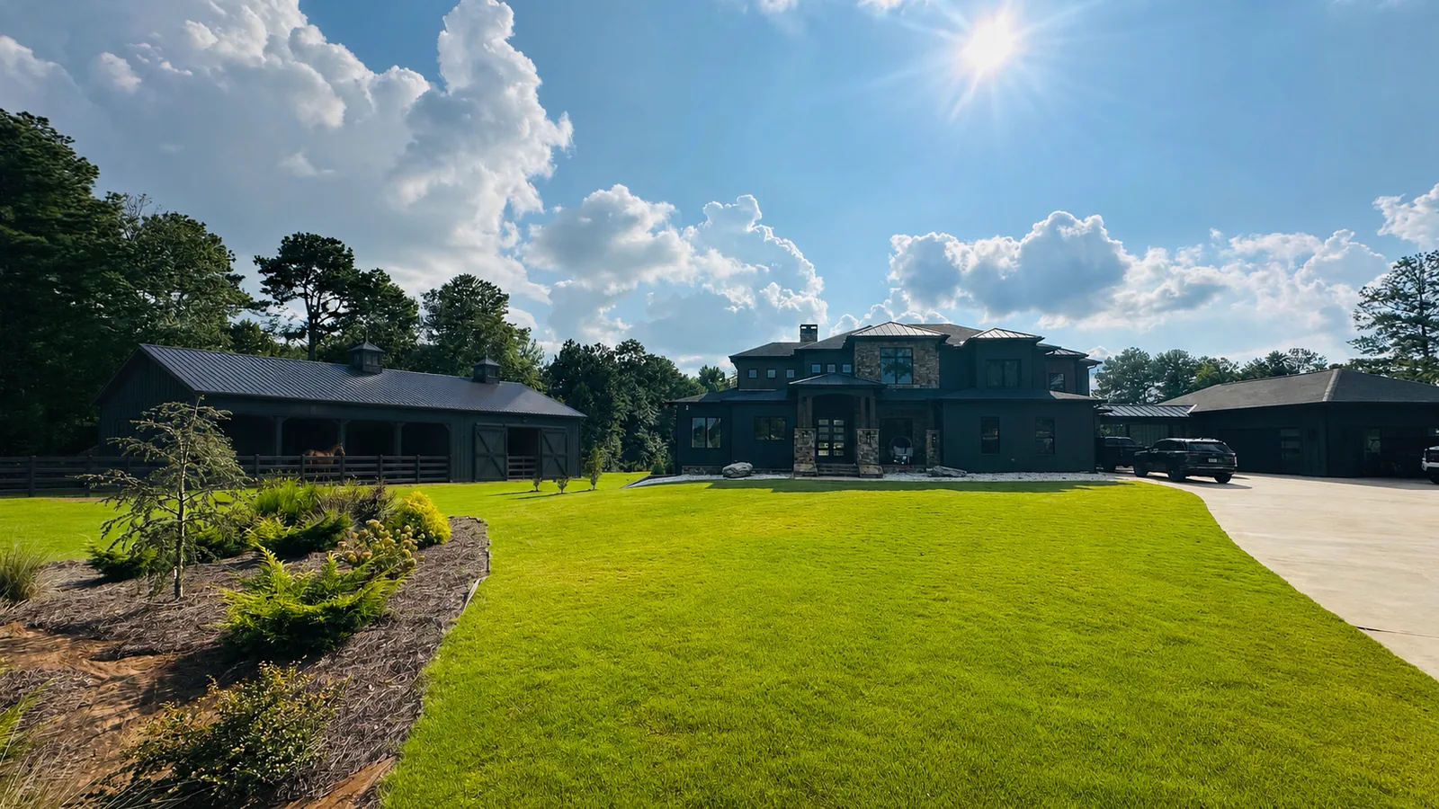 Black horse barn with covered stalls and board fencing beside the main house at Horse Boarding Georgia